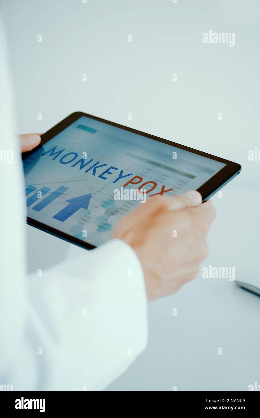 primo piano di un dottore, che indossa un cappotto bianco, nel suo ufficio, avendo un tablet digitale nelle sue mani con il testo scimmipox nel suo schermo Foto Stock