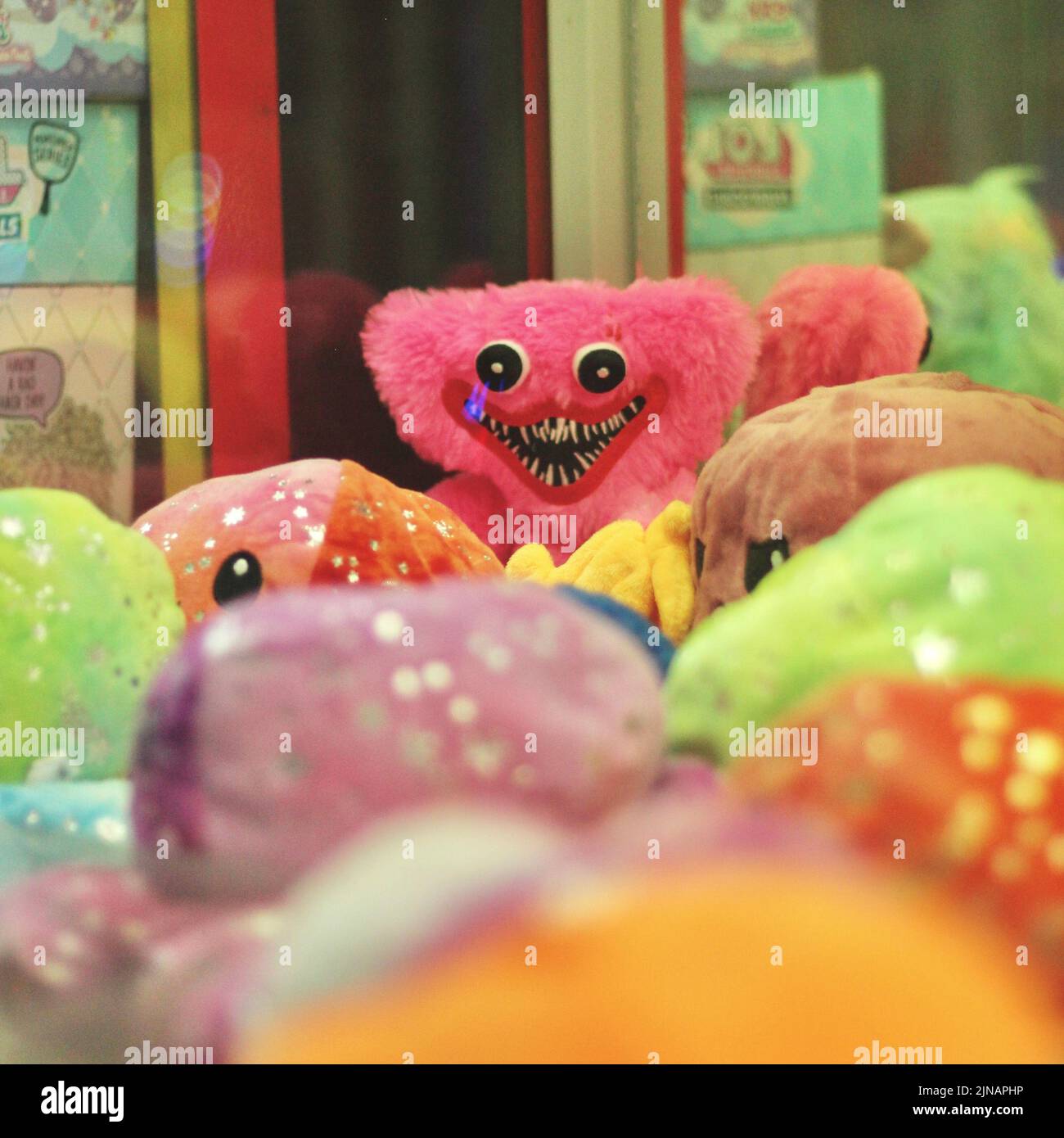 Massa giocattolo colorata con un inquietante ma grazioso giocattolo rosa peluche guardando la macchina fotografica. Foto Stock