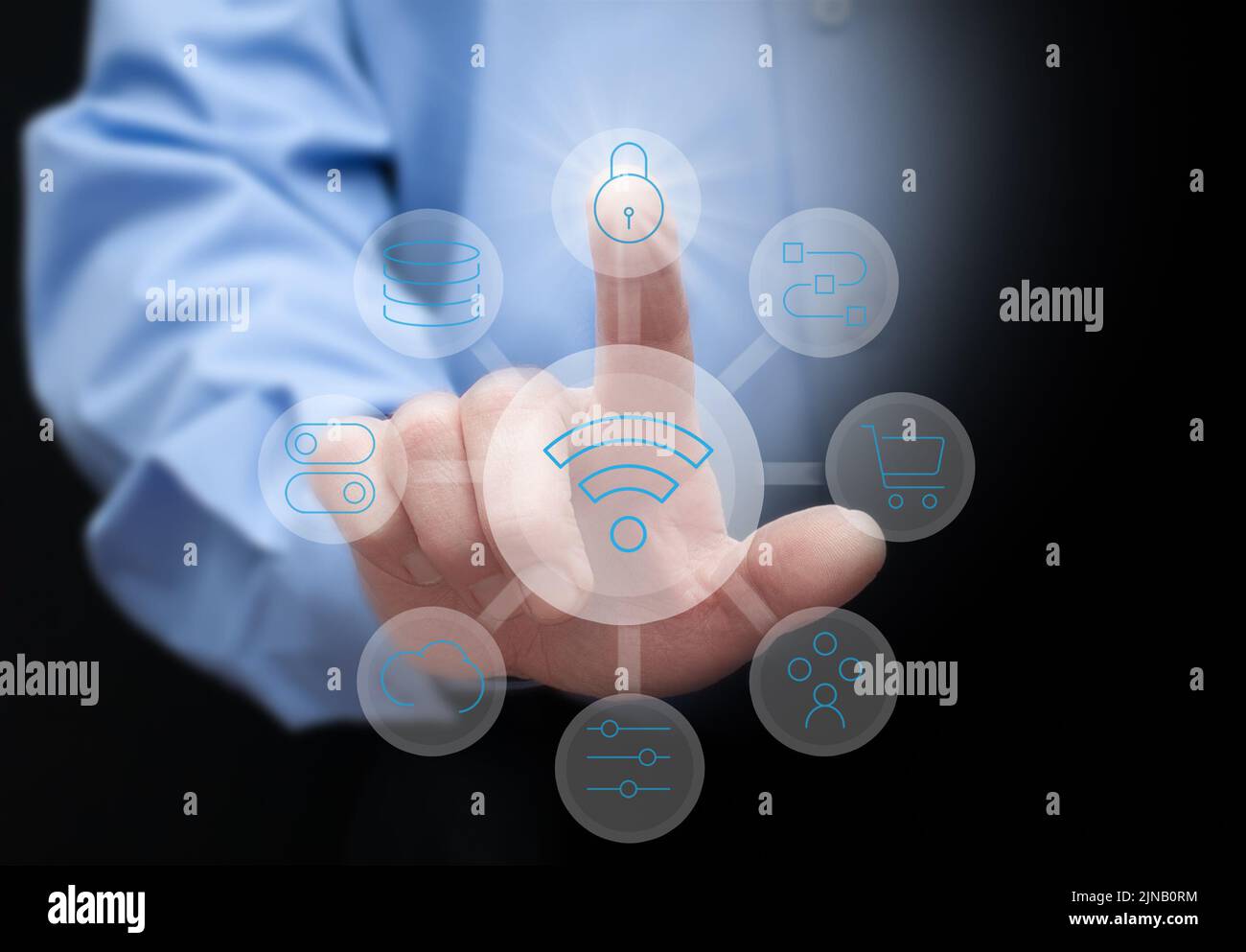 un uomo in una camicia blu su uno sfondo scuro preme pulsanti virtuali con simboli di archiviazione su cloud, protezione dei dati, shopping online e altri moderni te Foto Stock