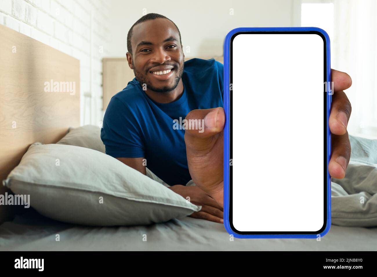 Happy Black Man che mostra il grande schermo del telefono sdraiato in camera da letto Foto Stock