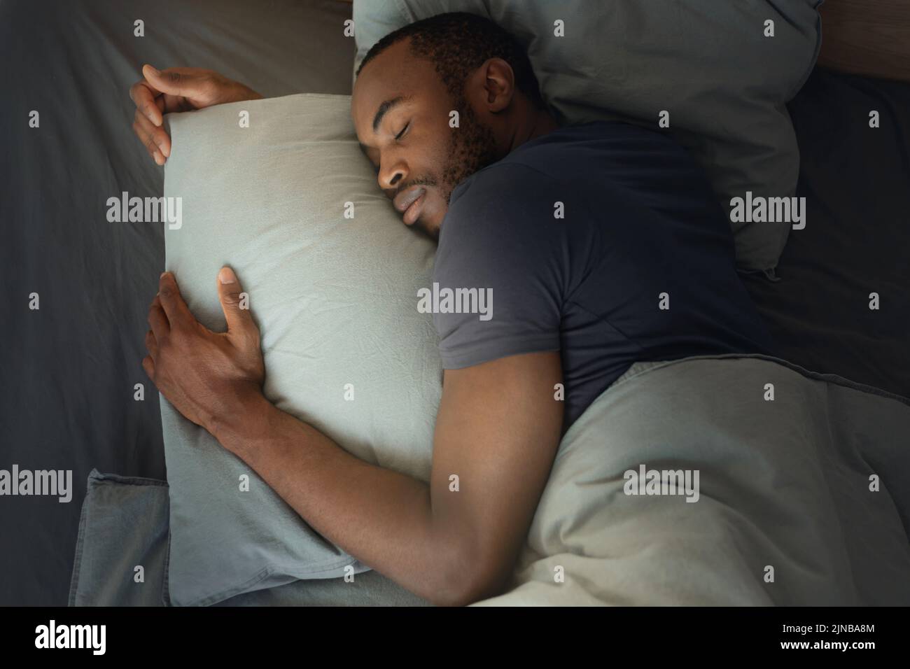 Vista dall'alto dell'uomo africano che dorme abbracciando il cuscino nella camera da letto Foto Stock