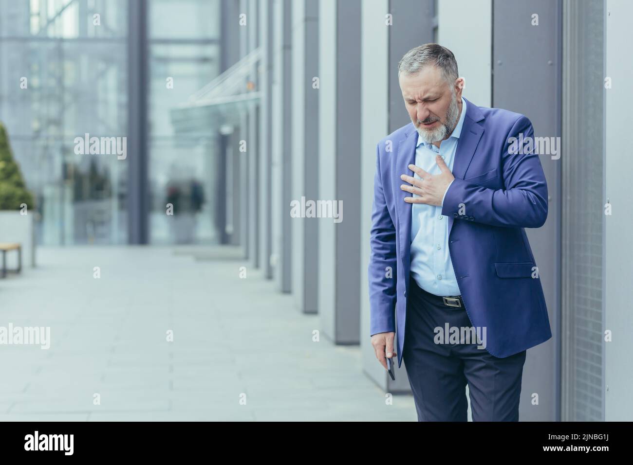 Il capo del banchiere grigio-haired anziano malato fuori dell'edificio dell'ufficio, banchiere ha dolore toracico severo, dolori di cuore Foto Stock