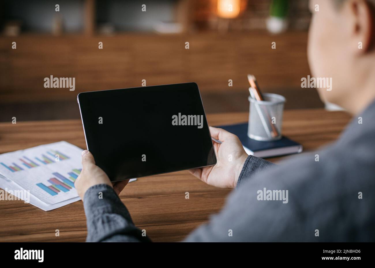 Un uomo giapponese adulto ha una videochiamata sul tablet con schermo vuoto al tavolo all'interno dell'ufficio, sul retro Foto Stock