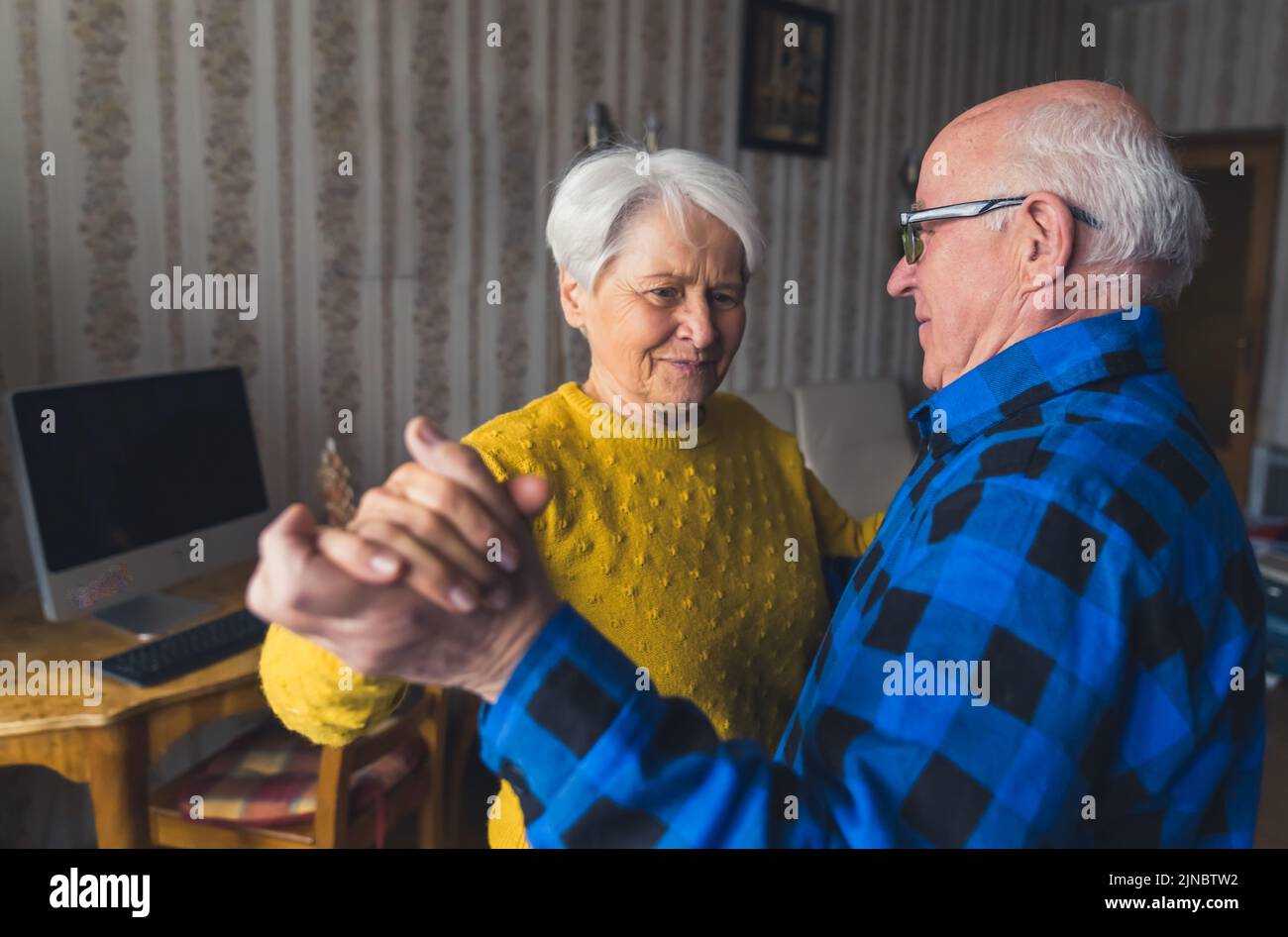 Felice donna anziana caucasica che balla insieme con suo marito nel soggiorno della propria casa. Foto di alta qualità Foto Stock