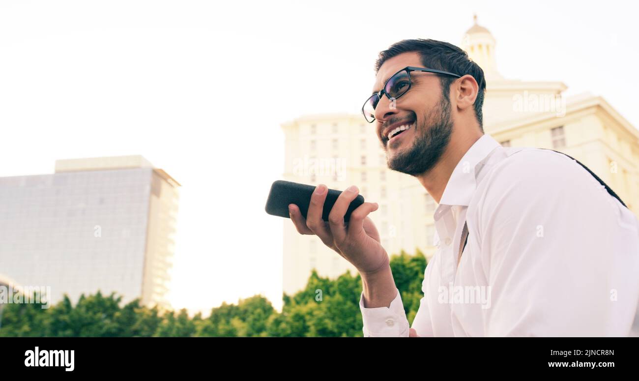 Spero che tu possa sentirmi forte e chiaro: Un bel giovane uomo d'affari che usa il suo cellulare per fare una nota vocale mentre cammina per la città. Foto Stock
