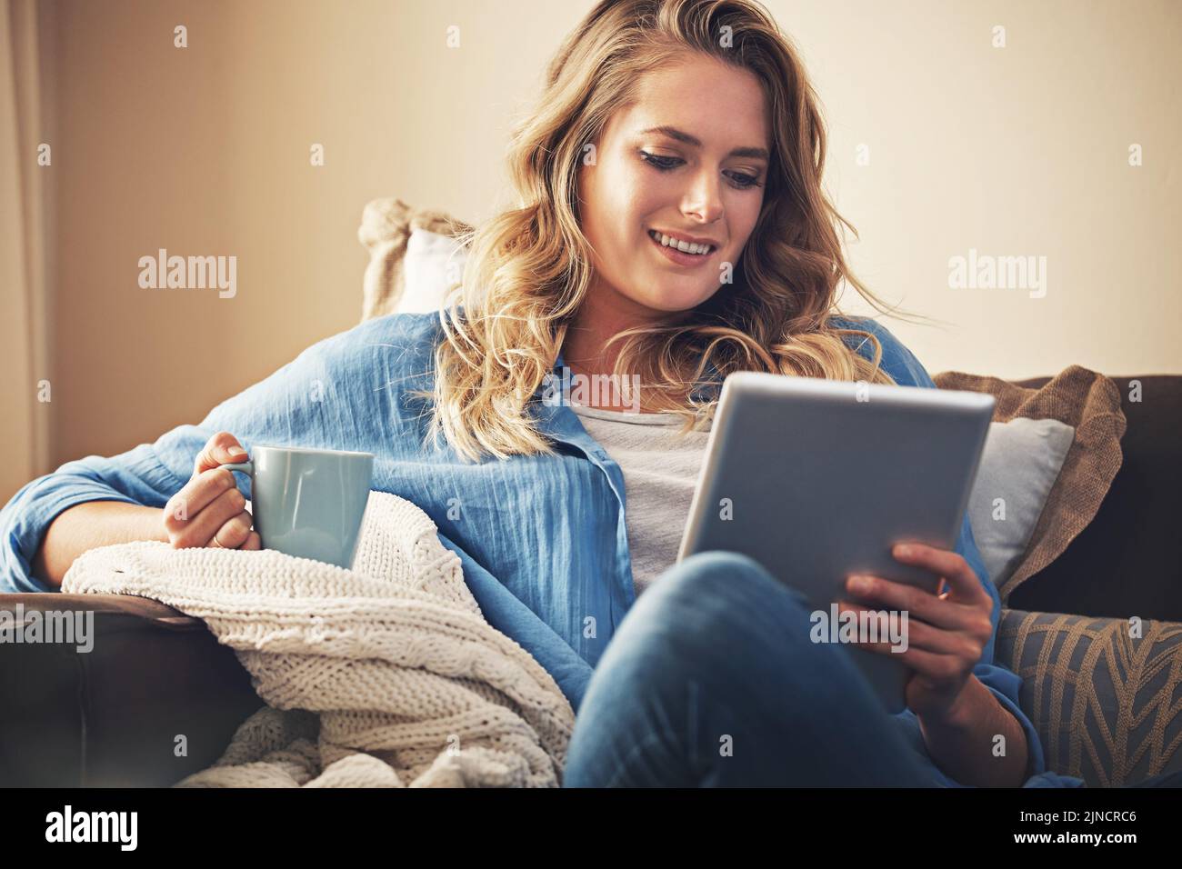 Intrattenimento wireless per tutto il fine settimana. Una giovane donna rilassata che ha un caffè e utilizza un tablet digitale sul divano di casa. Foto Stock