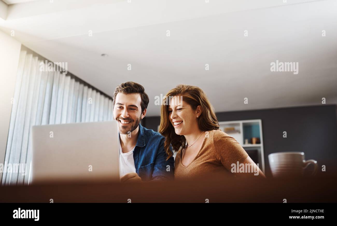 L'intrattenimento ti sorride su entrambi i volti. Una giovane coppia che guarda i video online insieme mentre fa il budget mensile a casa. Foto Stock