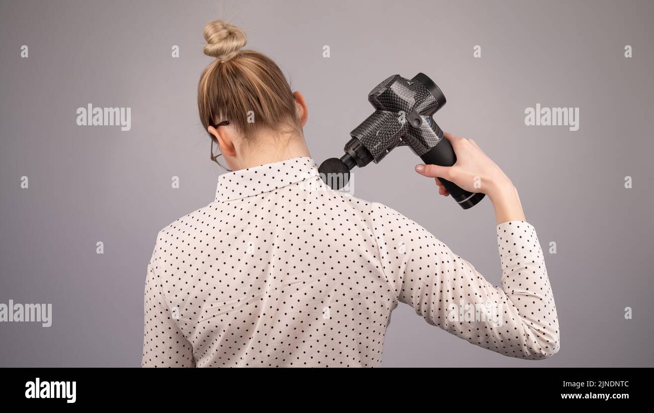 La signora caucasica si fa un massaggio alla schiena con una pistola massaggiatore su sfondo bianco. Foto Stock