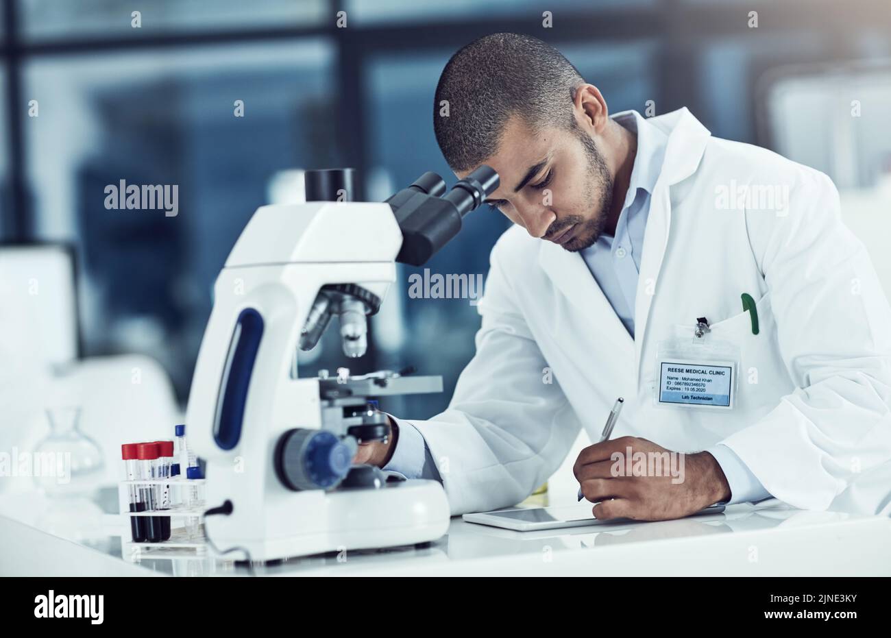 Serio scienziato maschile scrivere su un tablet per un dottorato online di ricerca in un laboratorio. Lavoratore di laboratorio che lavora su dati sanitari per una rivista scientifica Foto Stock