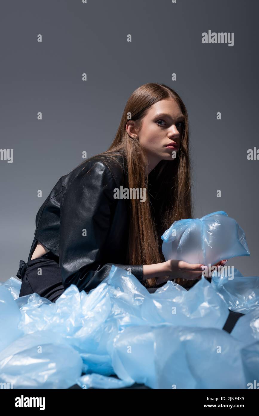 modello a brunetta in elegante abito nero che posa intorno a borse di plastica blu sul grigio Foto Stock
