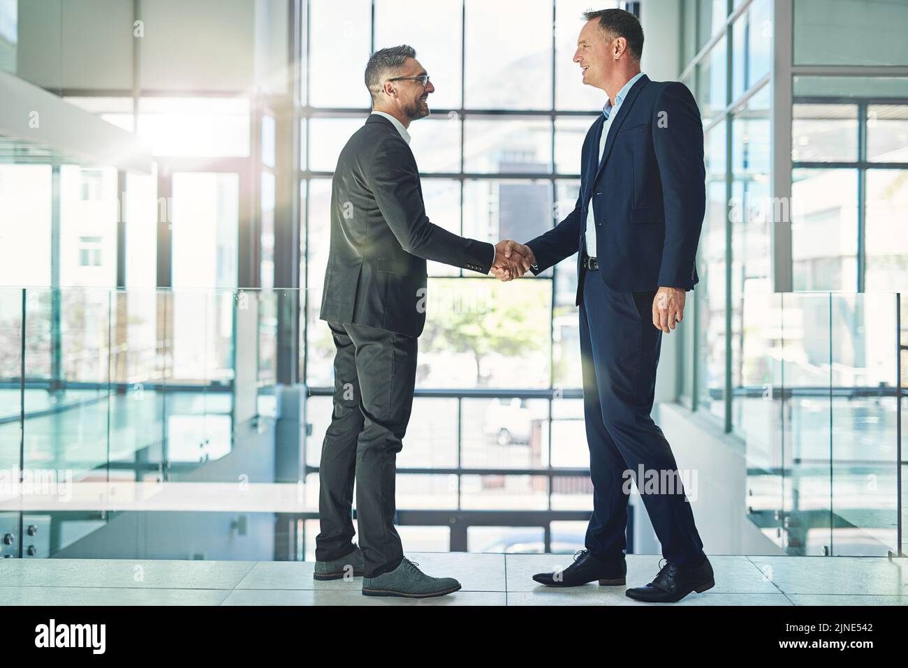 Uomini d'affari aziendali fiduciosi e sorridenti si scambiano le mani in una riunione di fusione globale di fiducia in azienda moderna. Dirigente professionista Foto Stock