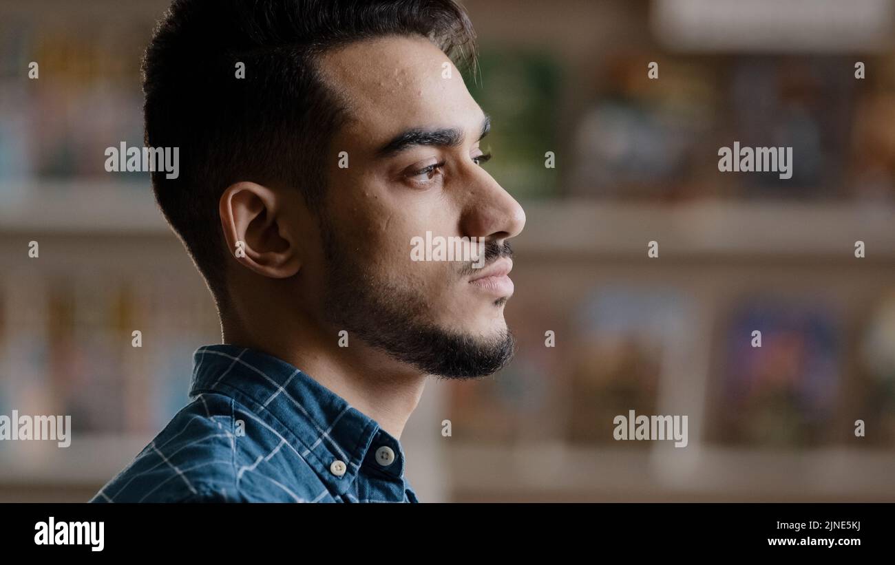 Ritratto di giovane uomo modello arabo serio con barba in camicia a plaid in piedi in casa posa guardando la macchina fotografica primo piano triste pene hispanic bello Foto Stock