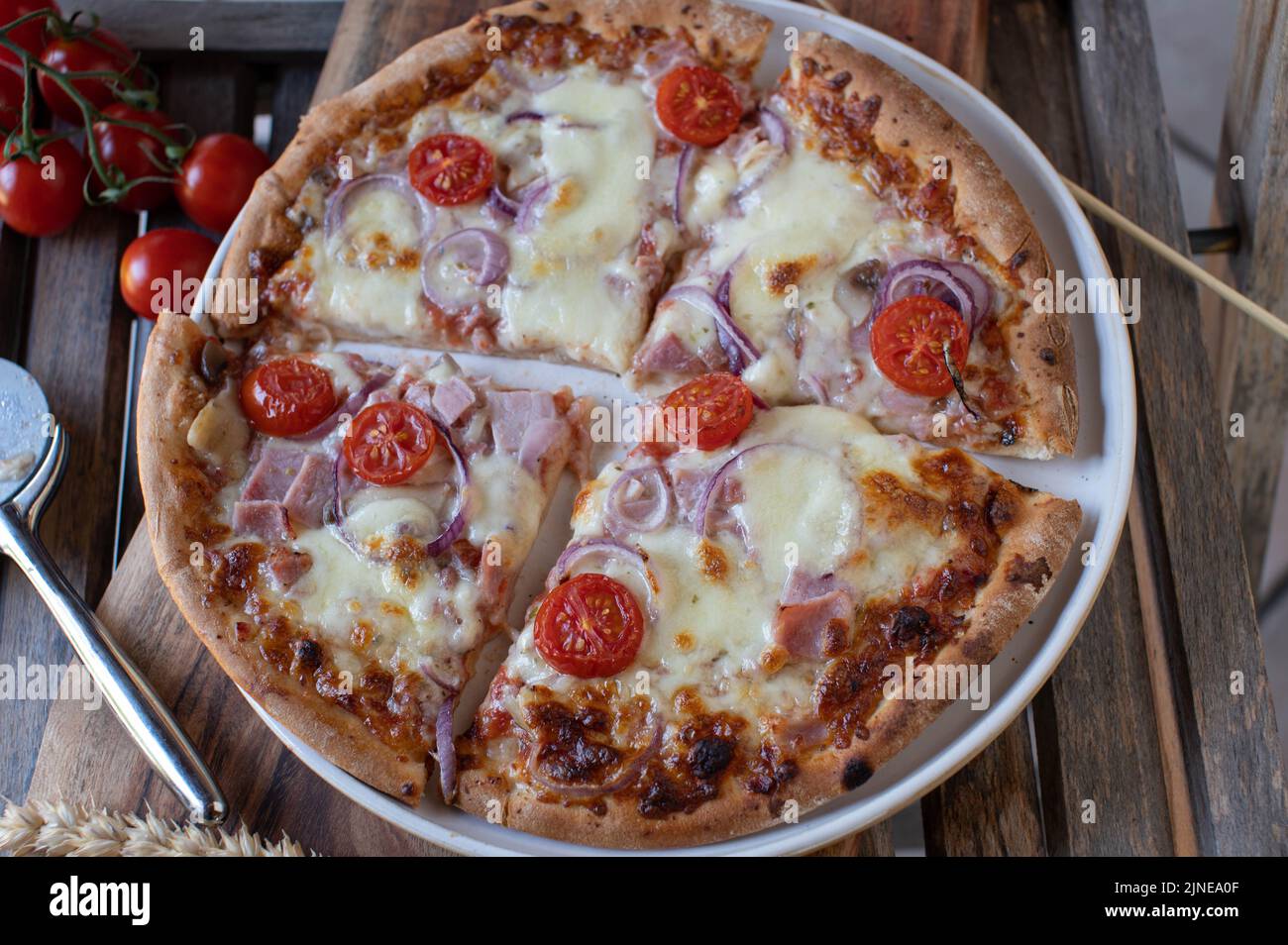 Pizza con prosciutto, mozzarella, cipolle rosse e pomodori su un piatto Foto Stock