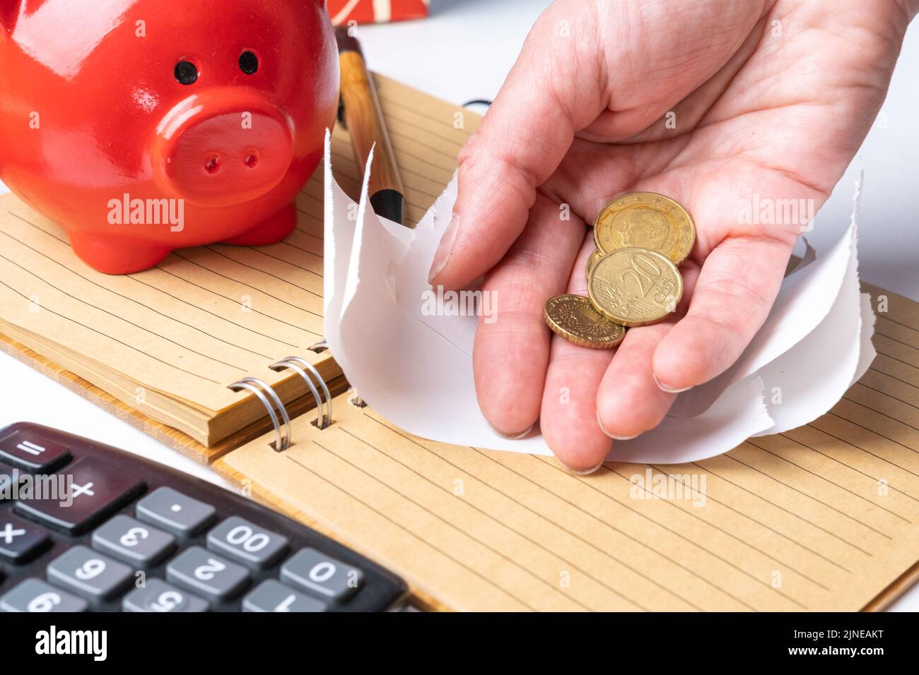 Una mano di una donna anziana che tiene piccole monete estratte da una banca di porcellini, un assegno vuoto, una calcolatrice, primo piano. Il concetto di spese di pianificazione, taxe Foto Stock