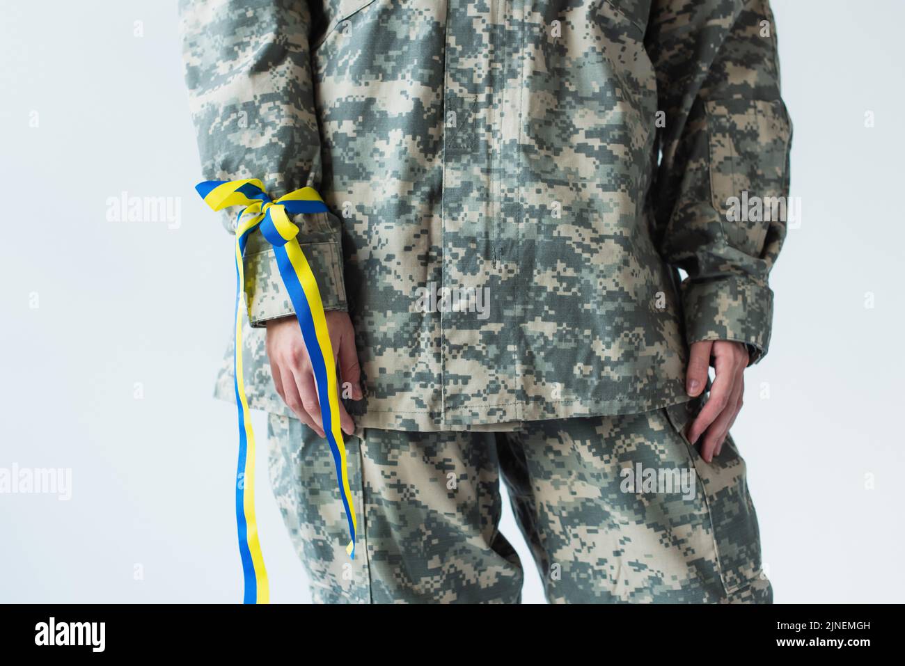 Vista ritagliata del soldato in uniforme con nastro blu e giallo a mano isolato su grigio, immagine stock Foto Stock