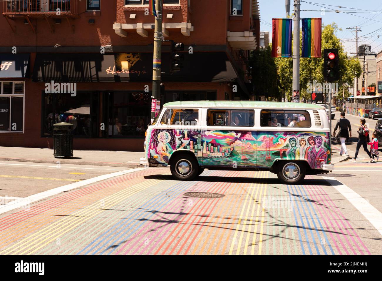 L'iconico pulmino dell'epoca VW 70-s Hippie guidando sulla strada sopra una croswalk color arcobaleno nel quartiere di Castro, famoso per la sua cultura LGBTQ, a San Francisco Foto Stock