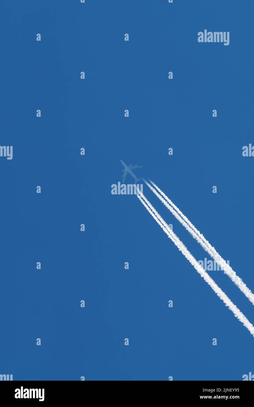 Velivolo passeggeri su un cielo blu con tracce visibili di condensa di vapore acqueo e carburante bruciato. Concetto di viaggio, traffico aereo e ambiente Foto Stock