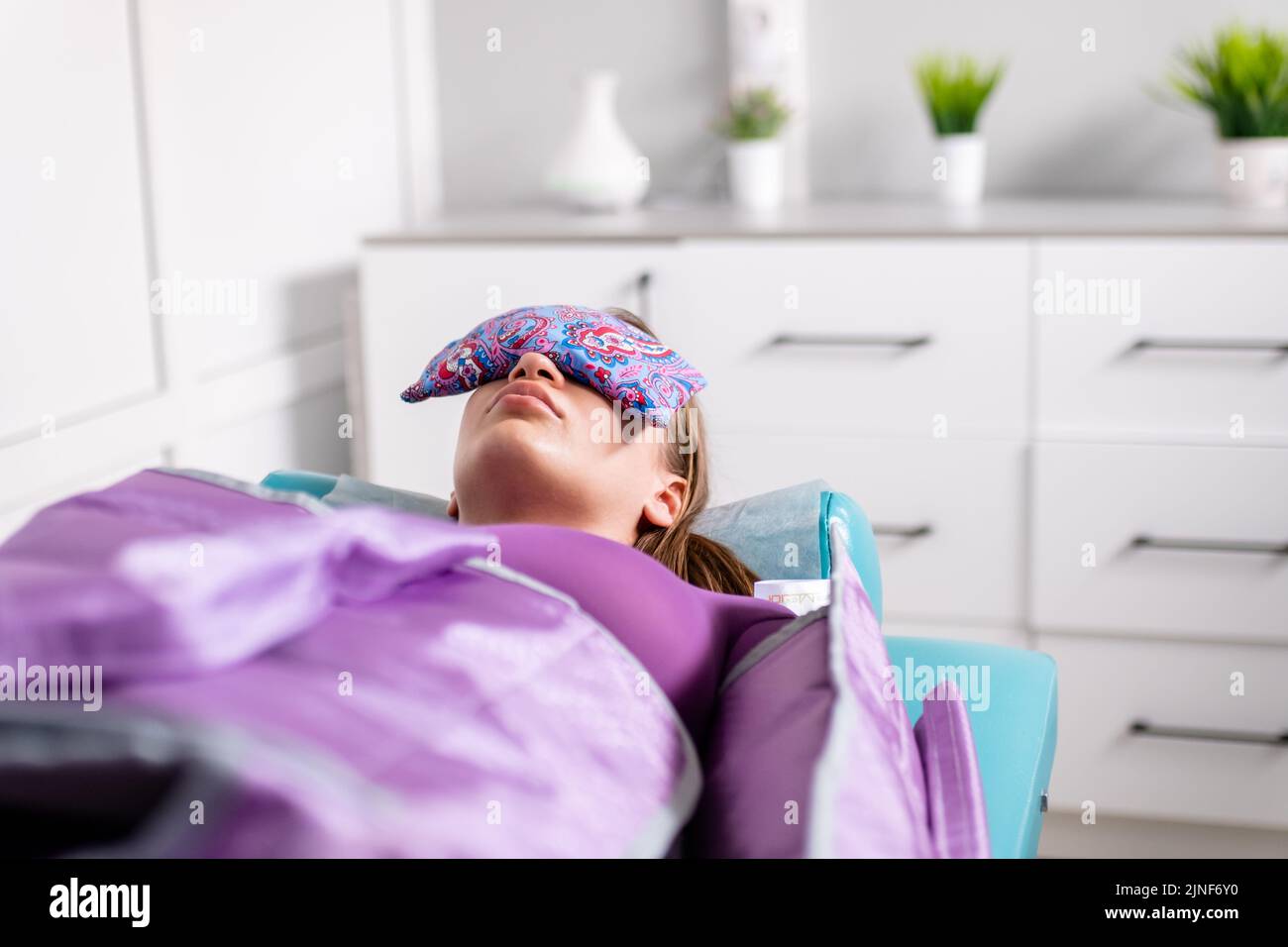 Donna sdraiata con gli occhi chiusi durante la sessione di pressoterapia in clinica di bellezza. Concetto Foto Stock