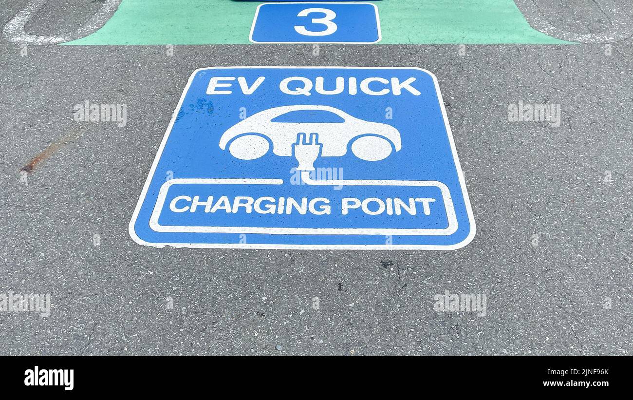 Un cartello per un caricabatterie rapido EV sul pavimento di un parcheggio sul tetto presso un centro commerciale EON, blu e bianco, con una spina e un'auto Foto Stock