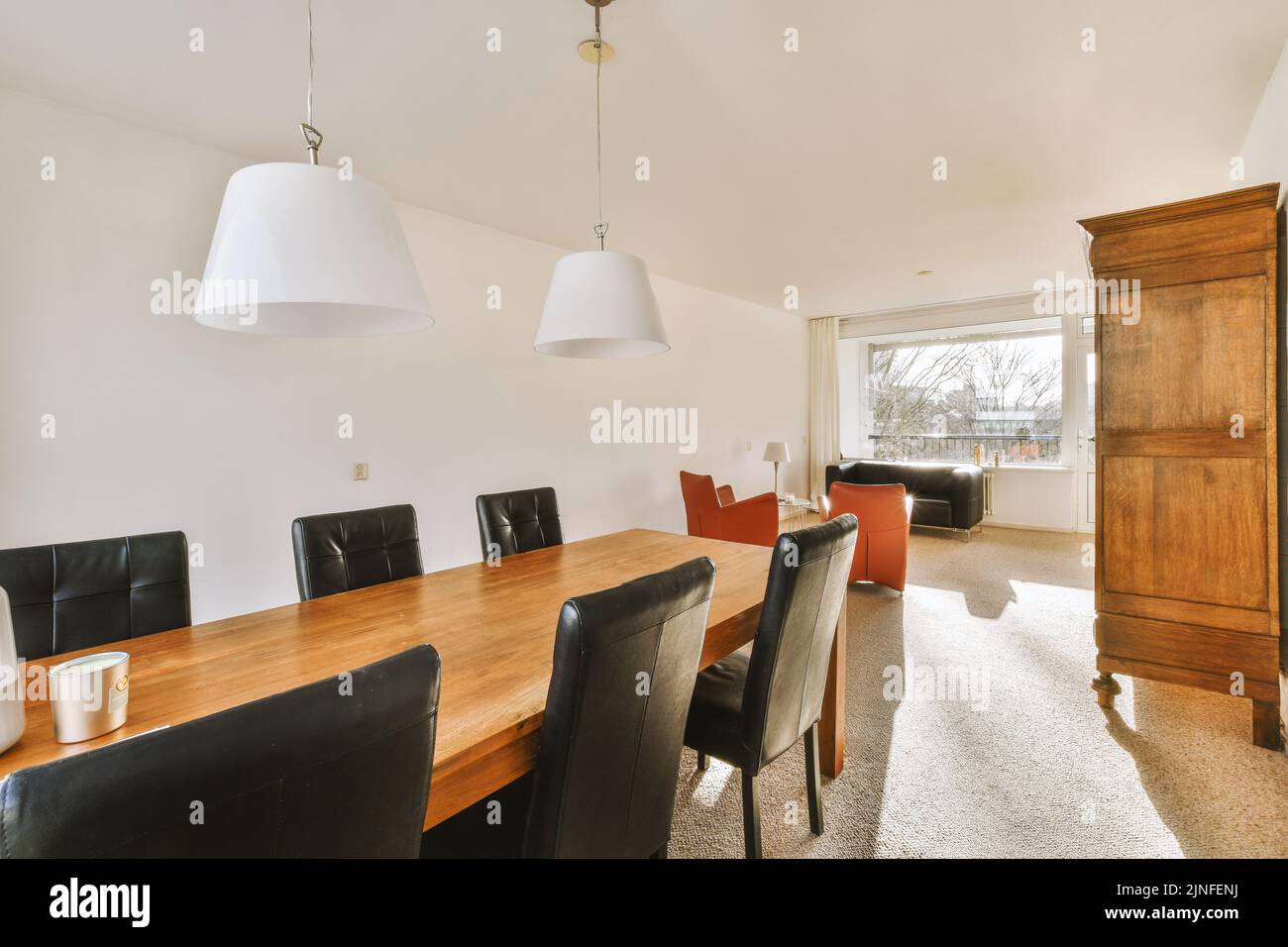 Sedie confortevoli e tavolo in legno posto sotto eleganti lampade contro la parete con armadio in sala da pranzo Foto Stock