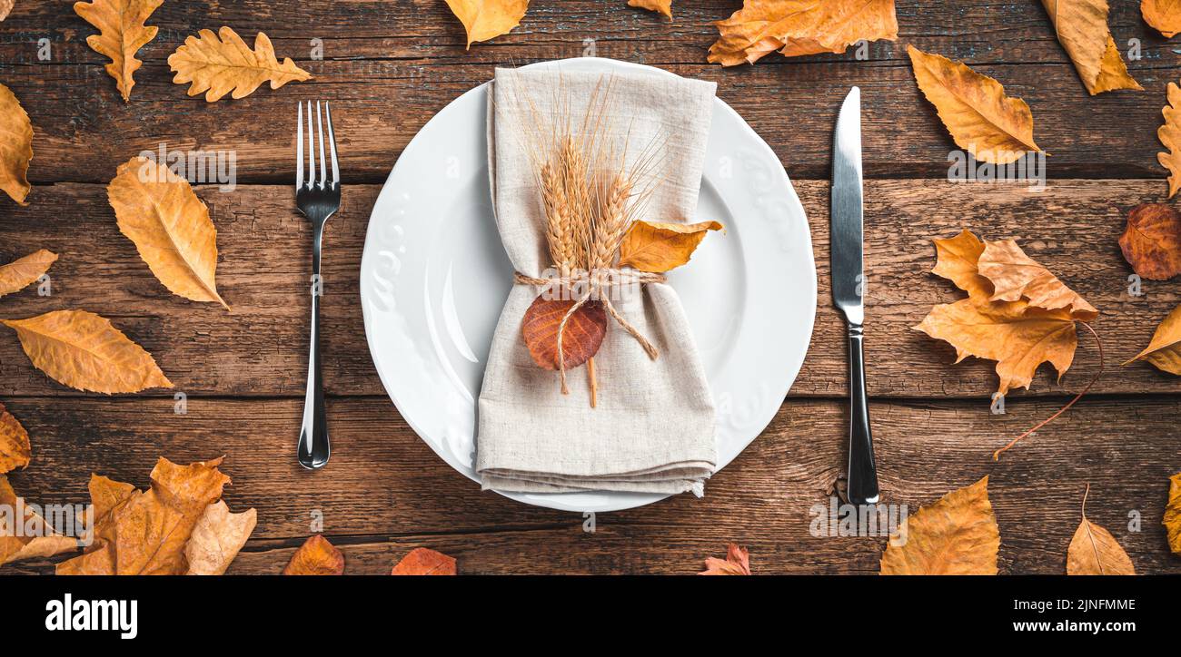 Sfondo autunnale con posate, piatti e foglie autunnali su sfondo ligneo. Foto Stock