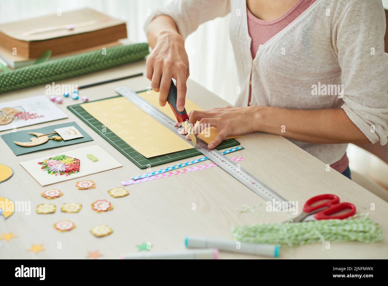 Donna creativa seduta al tavolo di legno e facendo biglietti d'auguri per i suoi amici, scrapbooking elementi sdraiati su superficie Foto Stock