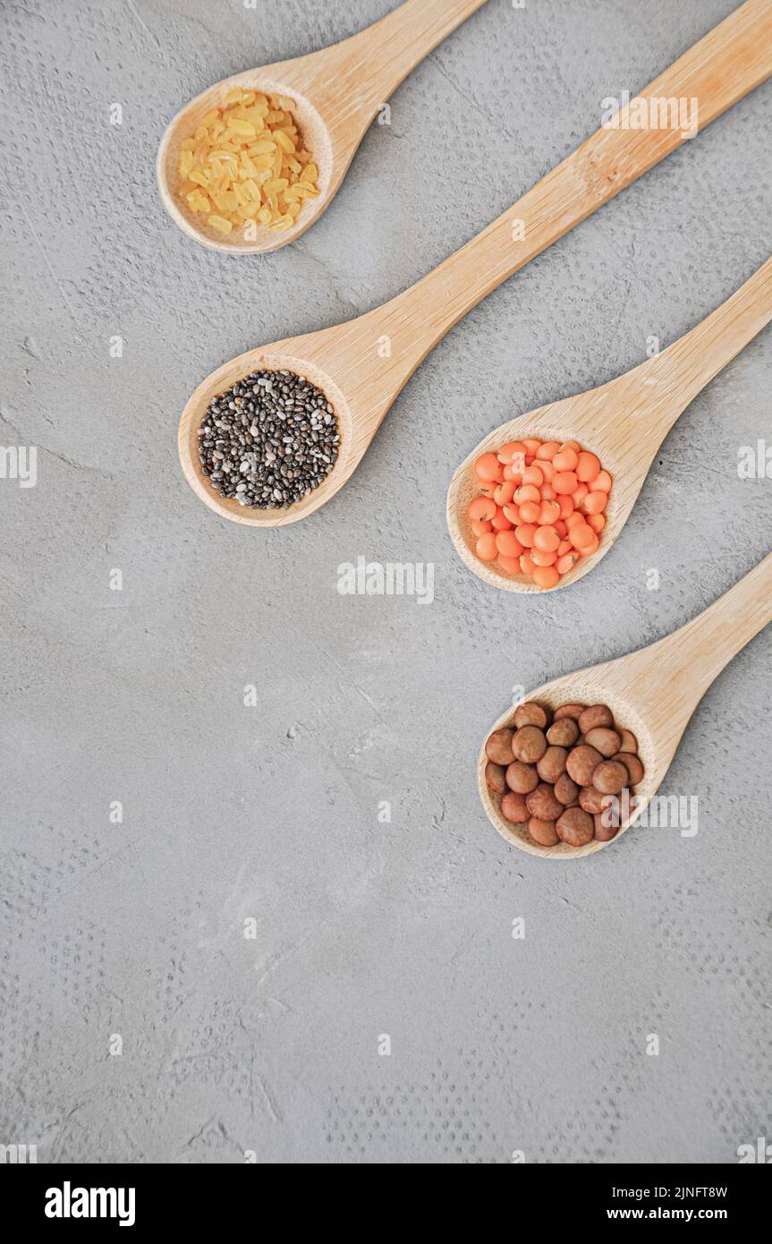 Diversi o vari tipi di fagioli secchi o legumi secchi in cucchiaio di legno su sfondo grigio. Grani interi, alimento sano e concetto di dieta. Vista dall'alto. FL Foto Stock