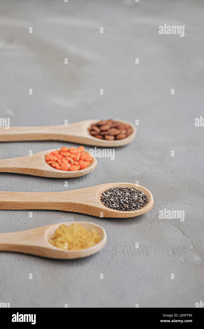 Diversi o vari tipi di fagioli secchi o legumi secchi in cucchiaio di legno su sfondo grigio. Grani interi, alimento sano e concetto di dieta Foto Stock