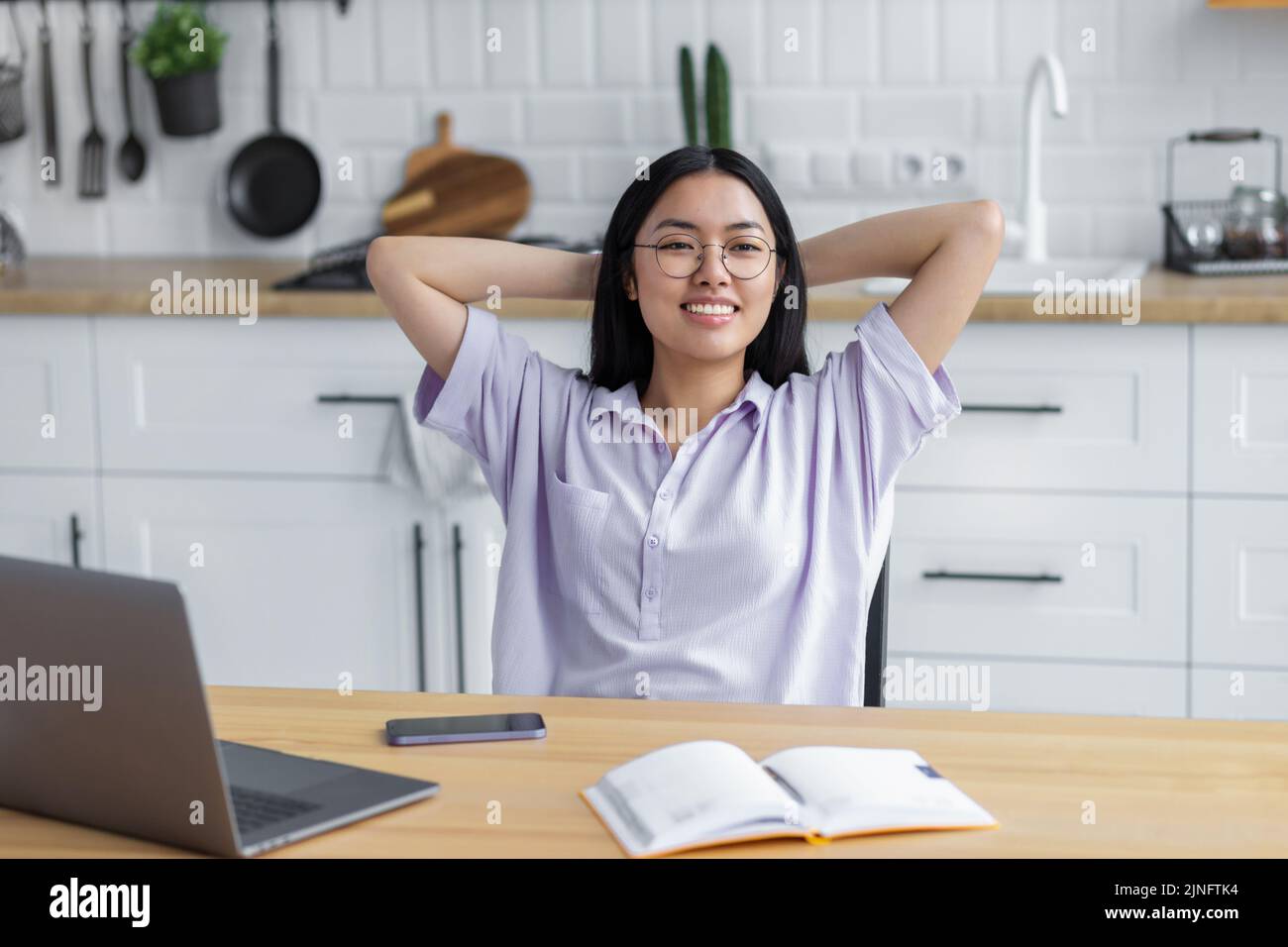 giovane freelance o studentessa donna seduta in ufficio a casa tenendo le mani dietro la testa pensando a qualcosa di bello. Foto Stock