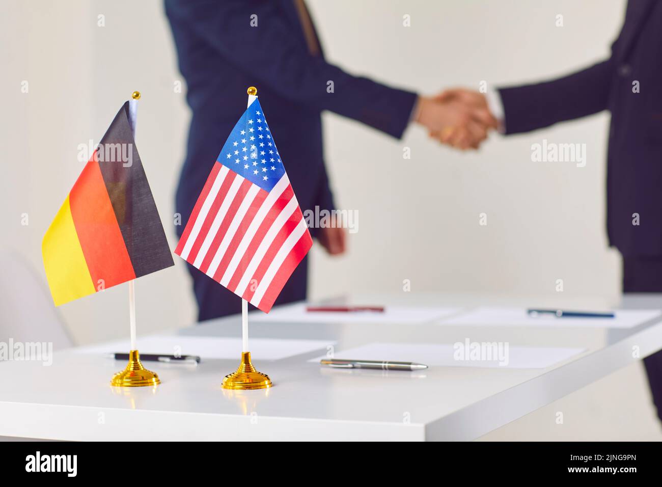 Piccole bandiere di Germania e Stati Uniti sono sul tavolo tra le mani di due politici. Foto Stock
