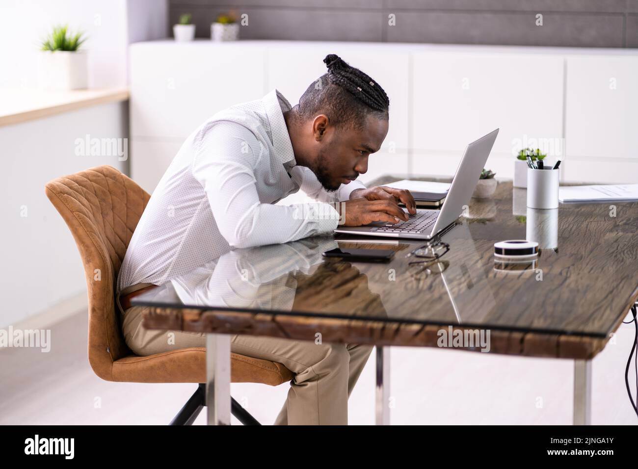 Uomo africano cattiva postura di lavoro digitando alla scrivania Foto Stock
