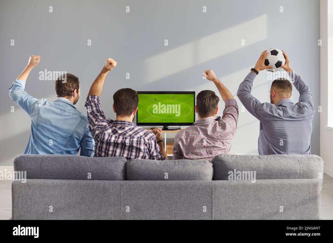 Vista posteriore degli amici maschi seduti sul divano a casa e guardando una partita di calcio in TV Foto Stock
