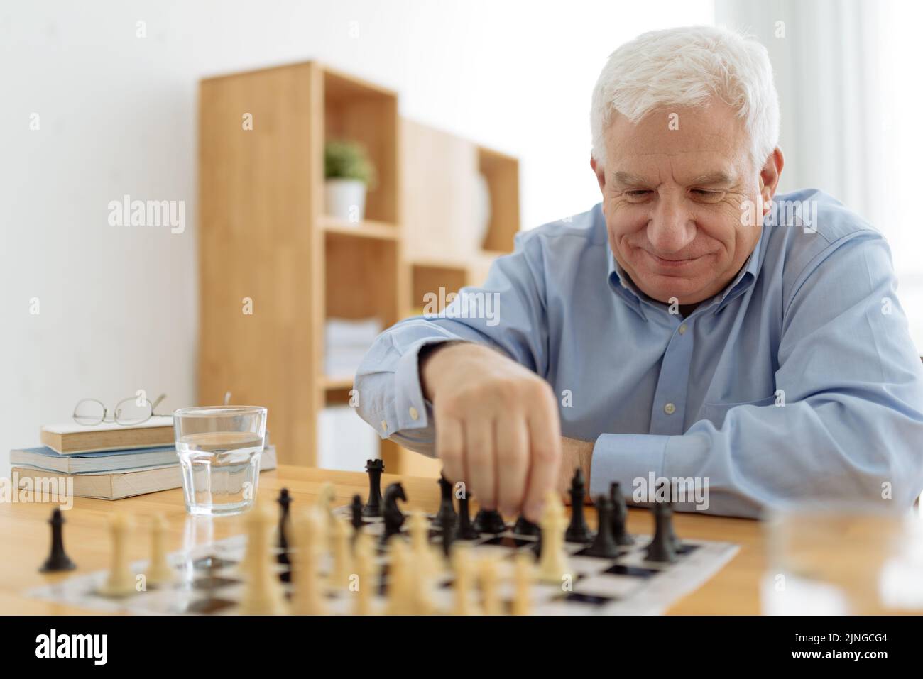 Uomo sorridente anziano che si diverse a giocare a scacchi in casa di cura Foto Stock