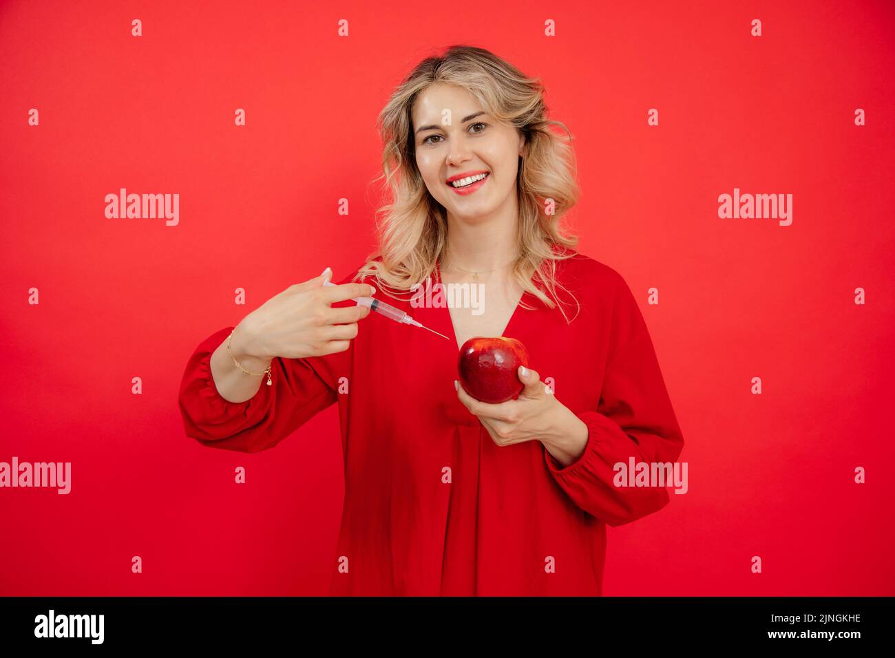 Donna sorridente mano attraente con siringa che applica l'iniezione a mela rossa fresca succosa in studio. Settore del ringiovanimento Foto Stock