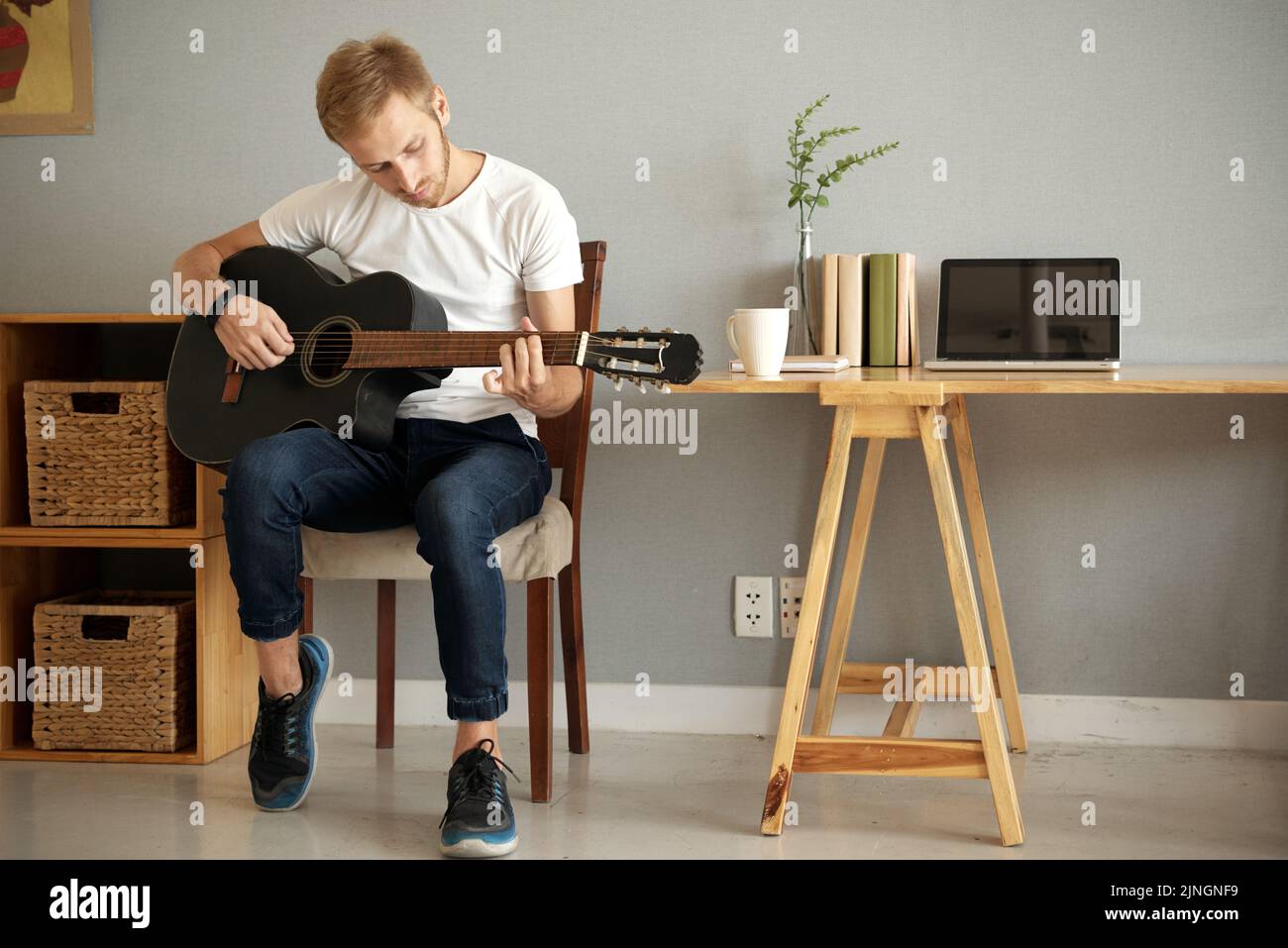 Giovane musicista che suona la chitarra acustica nel suo appartamento Foto Stock