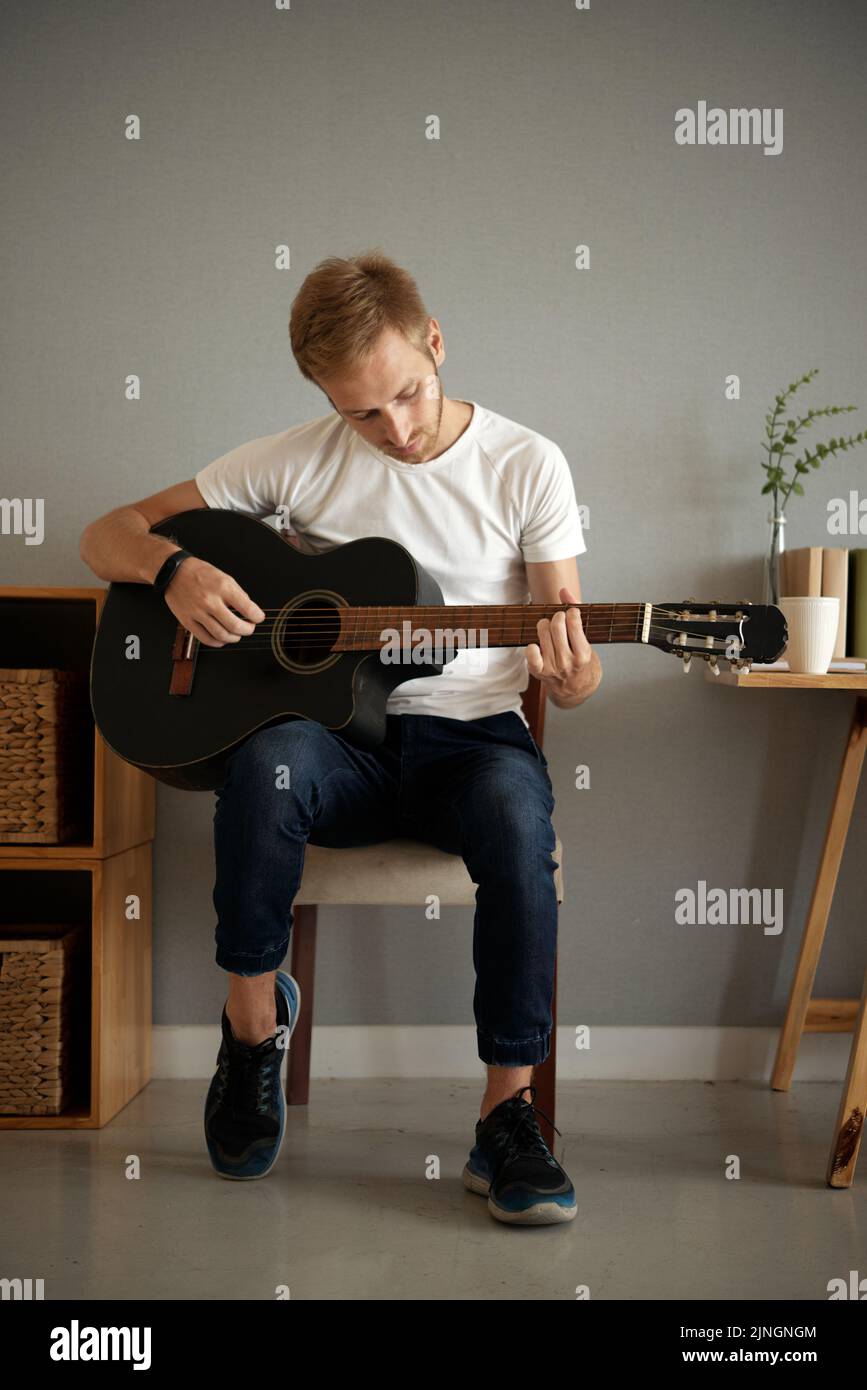 Giovane uomo che impara a suonare la chitarra acustica a casa Foto Stock