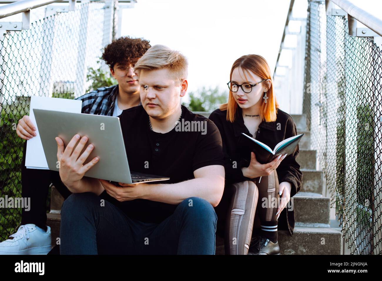 Gruppo di giovani studenti seduti su scale di cemento, guardando lo schermo del computer portatile. Un giovane uomo che tiene un notebook. Foto Stock