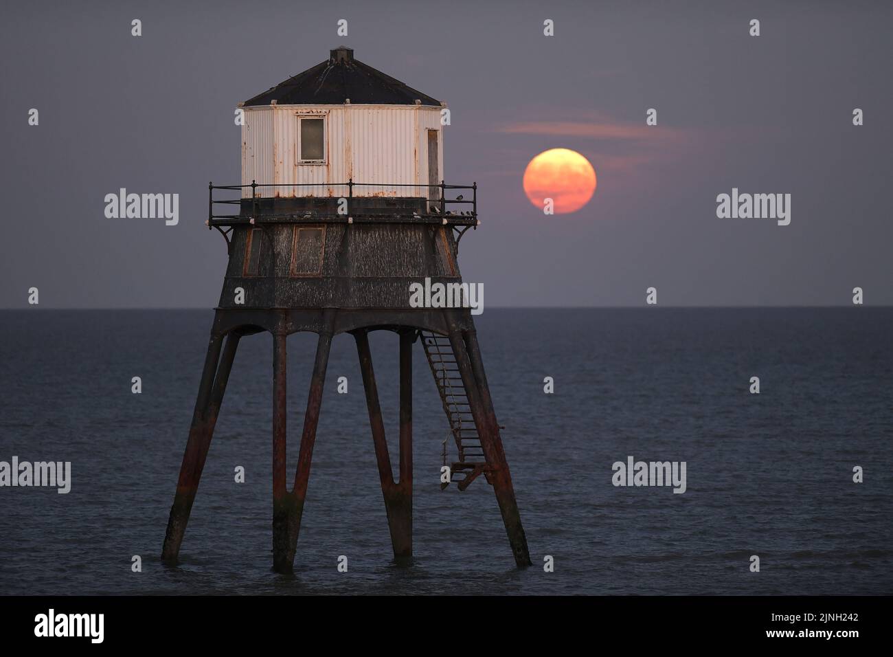 Dovercourt Essex, Regno Unito. 11th ago, 2022. L'intero Sturgeon Supermoon sorge dietro il faro inferiore di Dovercourt in Essex. La Luna piena di Agosto è chiamata la Luna di Sturgeon perché le tribù Algonquin del Nord America la chiamano dopo l'abbondanza di Sturgeon nei fiumi in questo periodo dell'anno. Credit: MARTIN DALTON/Alamy Live News Foto Stock