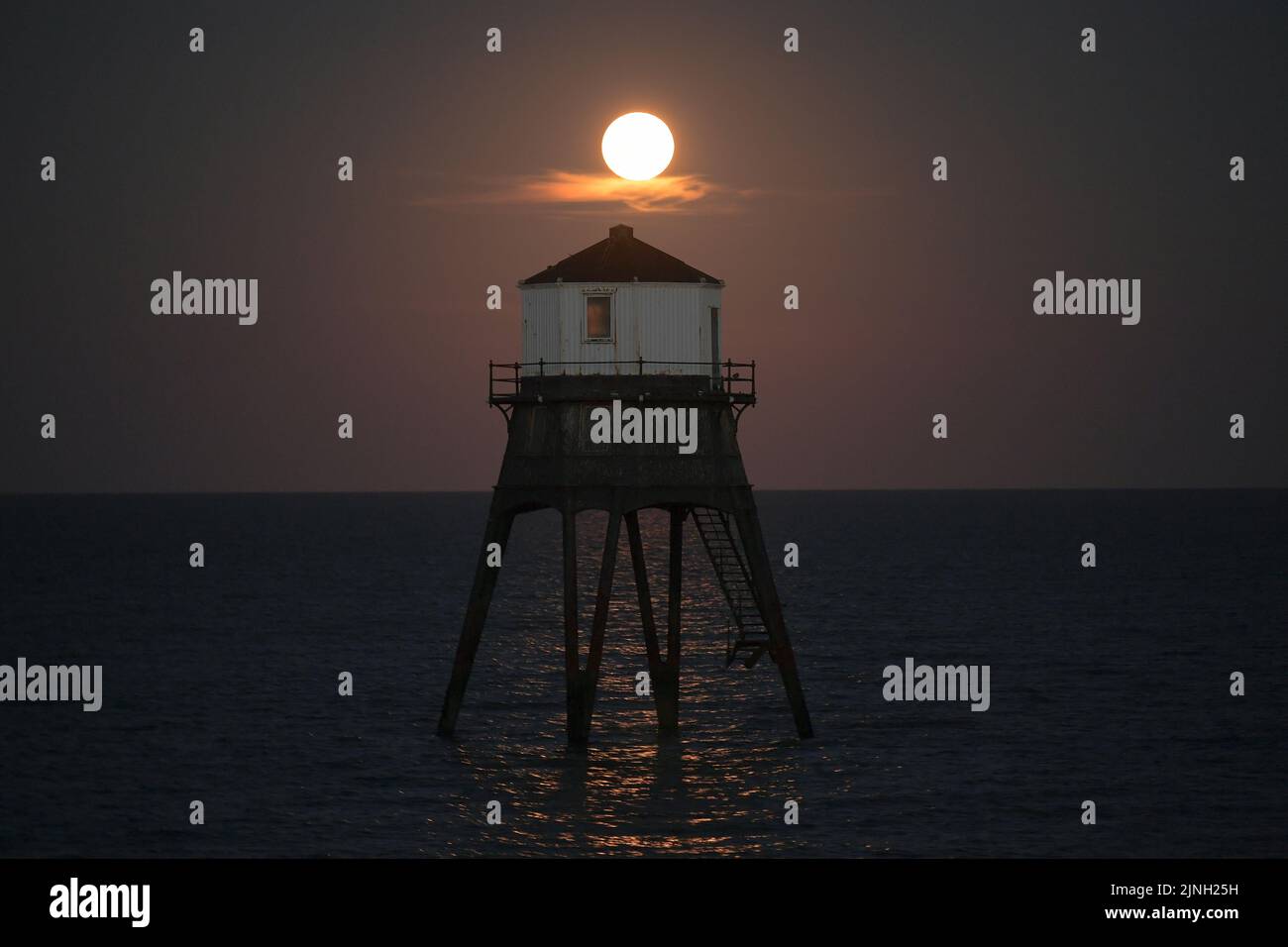Dovercourt Essex, Regno Unito. 11th ago, 2022. L'intero Sturgeon Supermoon sorge dietro il faro inferiore di Dovercourt in Essex. La Luna piena di Agosto è chiamata la Luna di Sturgeon perché le tribù Algonquin del Nord America la chiamano dopo l'abbondanza di Sturgeon nei fiumi in questo periodo dell'anno. Credit: MARTIN DALTON/Alamy Live News Foto Stock