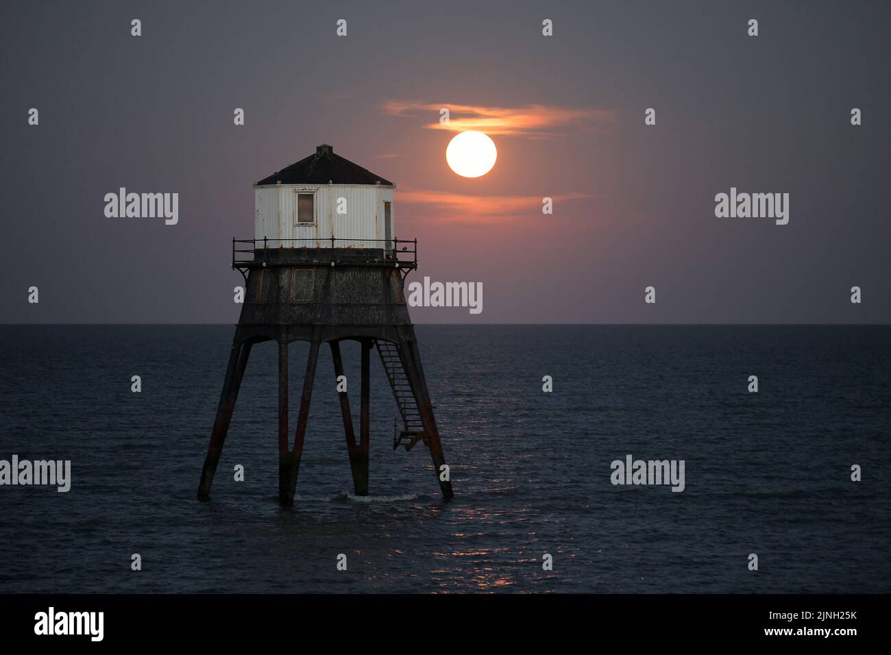 Dovercourt Essex, Regno Unito. 11th ago, 2022. L'intero Sturgeon Supermoon sorge dietro il faro inferiore di Dovercourt in Essex. La Luna piena di Agosto è chiamata la Luna di Sturgeon perché le tribù Algonquin del Nord America la chiamano dopo l'abbondanza di Sturgeon nei fiumi in questo periodo dell'anno. Credit: MARTIN DALTON/Alamy Live News Foto Stock
