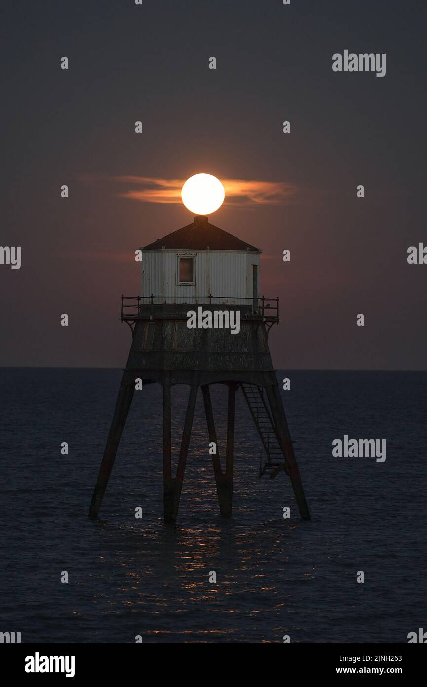 Dovercourt Essex, Regno Unito. 11th ago, 2022. L'intero Sturgeon Supermoon sorge dietro il faro inferiore di Dovercourt in Essex. La Luna piena di Agosto è chiamata la Luna di Sturgeon perché le tribù Algonquin del Nord America la chiamano dopo l'abbondanza di Sturgeon nei fiumi in questo periodo dell'anno. Credit: MARTIN DALTON/Alamy Live News Foto Stock