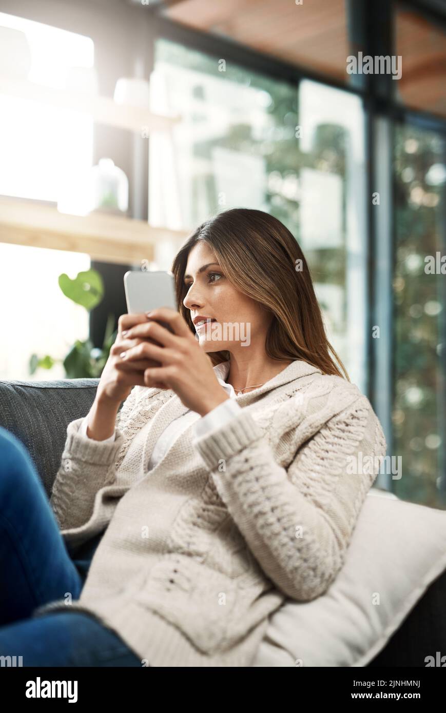 È troppo tardi per cambiare idea. Una giovane donna attraente che guarda premurosa e invia messaggi di testo mentre si rilassa sul suo divano a casa. Foto Stock