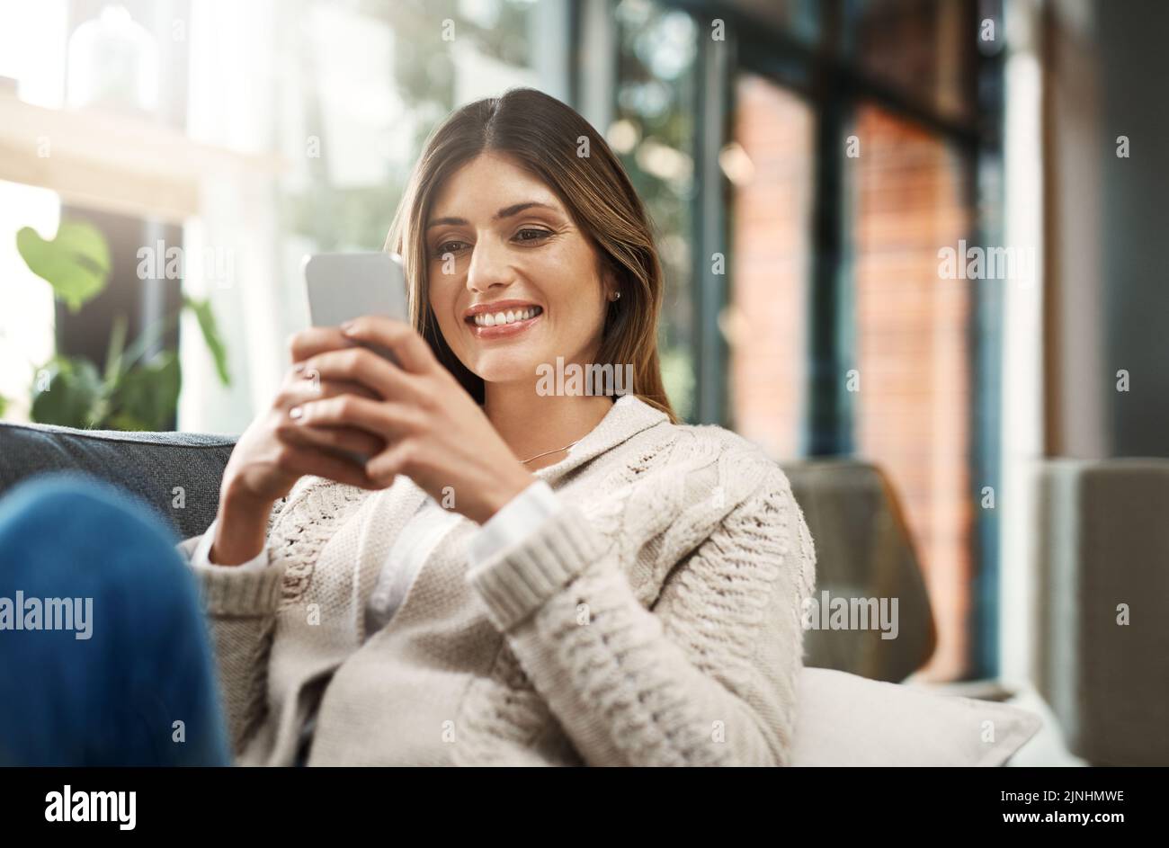 Forse dovrei pensare questo attraverso in primo luogo: Una giovane donna attraente che invia i messaggi di testo mentre si distendono sul suo divano a casa. Foto Stock