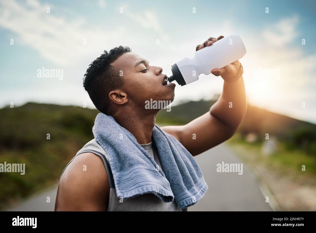 Rinfrescarsi dopo una corsa intensa. Un giovane sportivo che beve acqua mentre si esercita all'aperto. Foto Stock