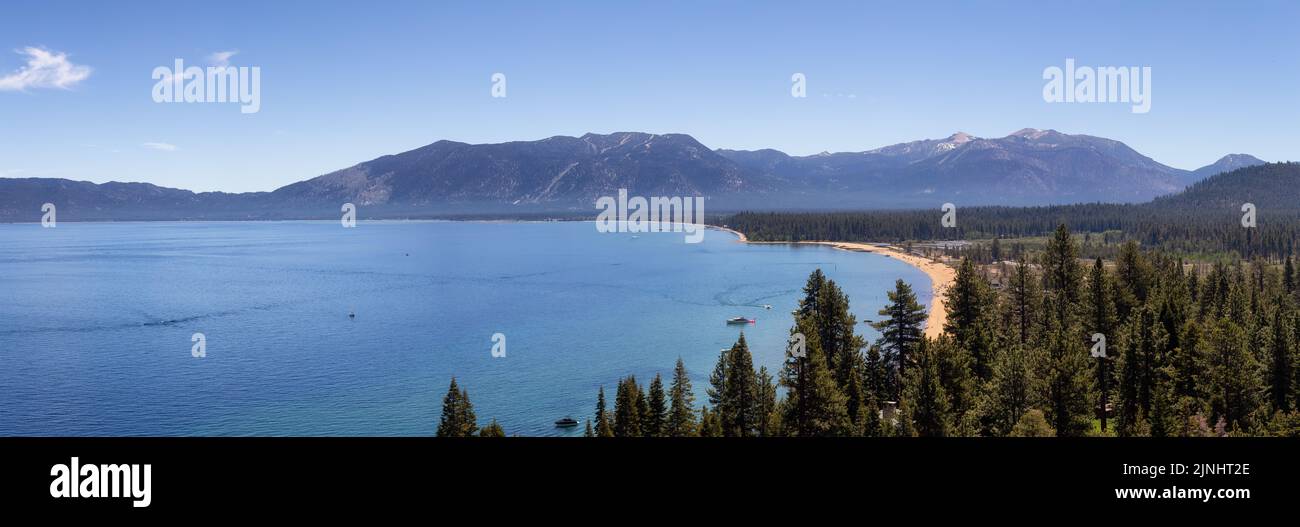 Vista panoramica del grande lago con spiaggia circondata da alberi e montagne. Foto Stock