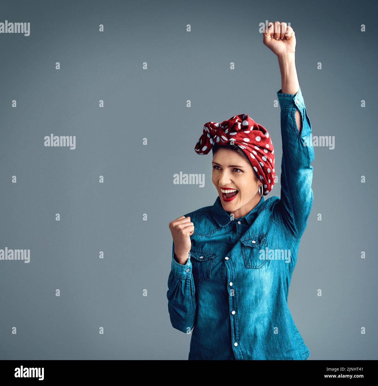 Un grande tifo per il femminismo. Studio shot di una giovane donna attraente in piedi con il braccio sollevato in celebrazione su uno sfondo grigio. Foto Stock