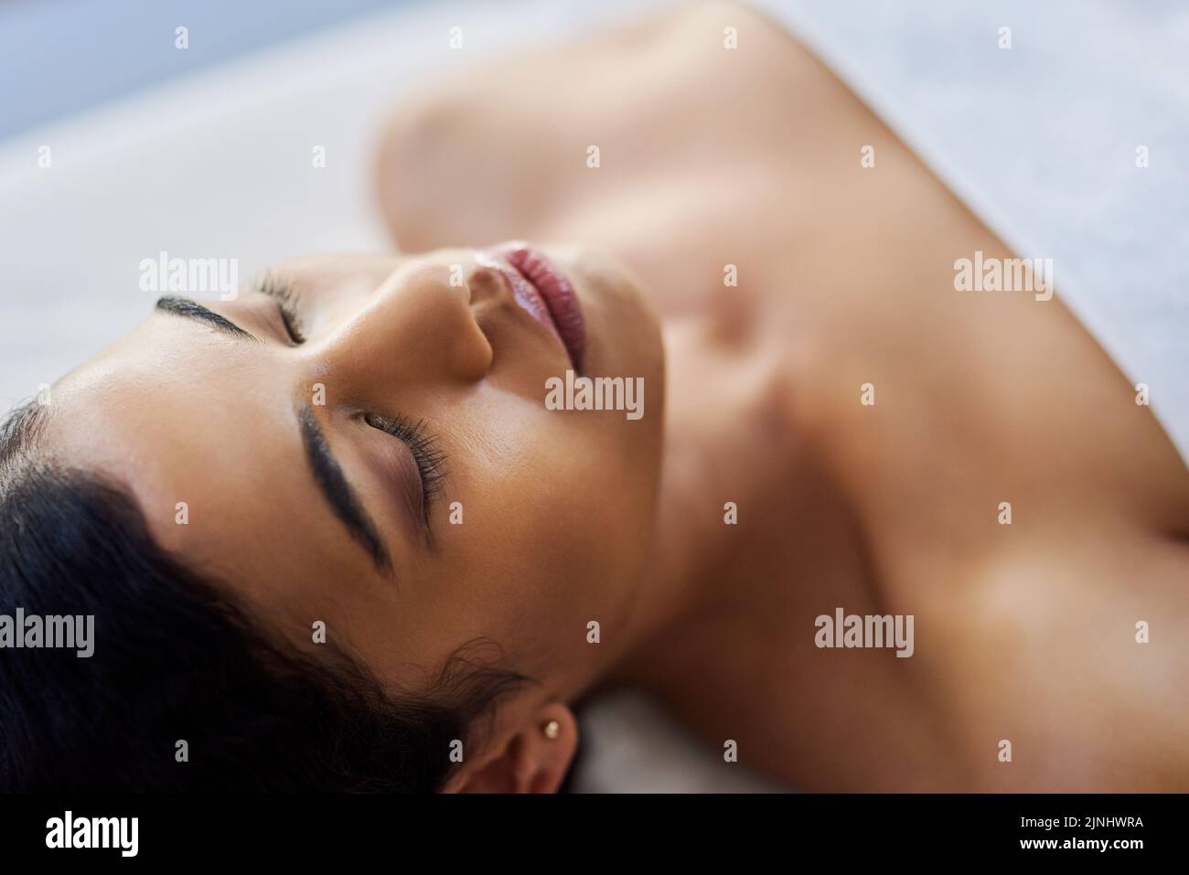 Quando gli effetti di una lussuosa esperienza spa indugiano, una giovane donna attraente che si rilassa su un tavolo da massaggio in una spa. Foto Stock