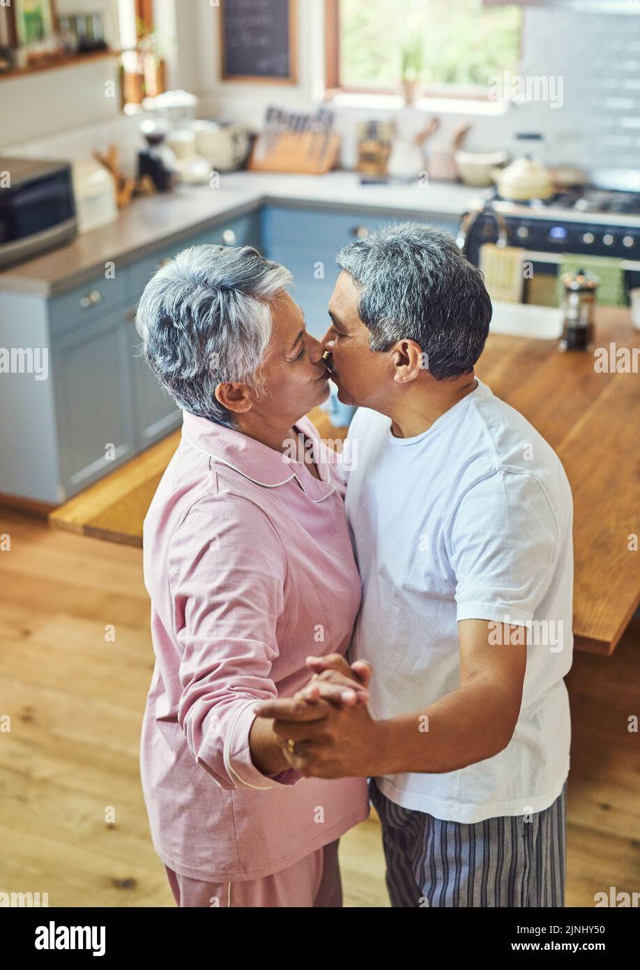 Hanno ancora le mosse, una coppia di anziani spensierati che ballano mentre condividono un bacio in cucina a casa durante il giorno. Foto Stock