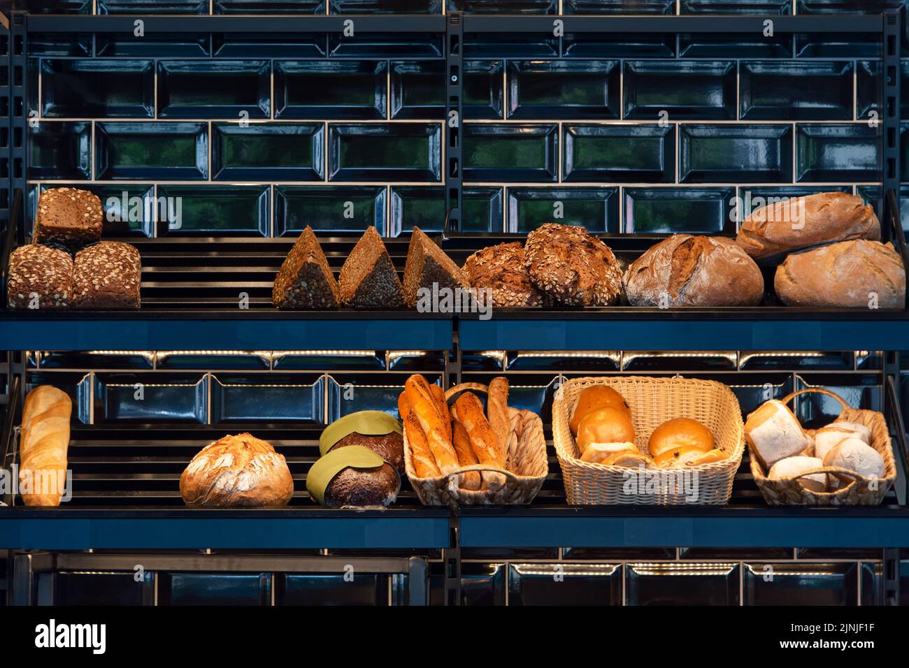 Pane appena sfornato su una mensa in panetteria, baguette e panini. Diversi tipi di deliziose forme di pane in un panificio tedesco. Foto Stock