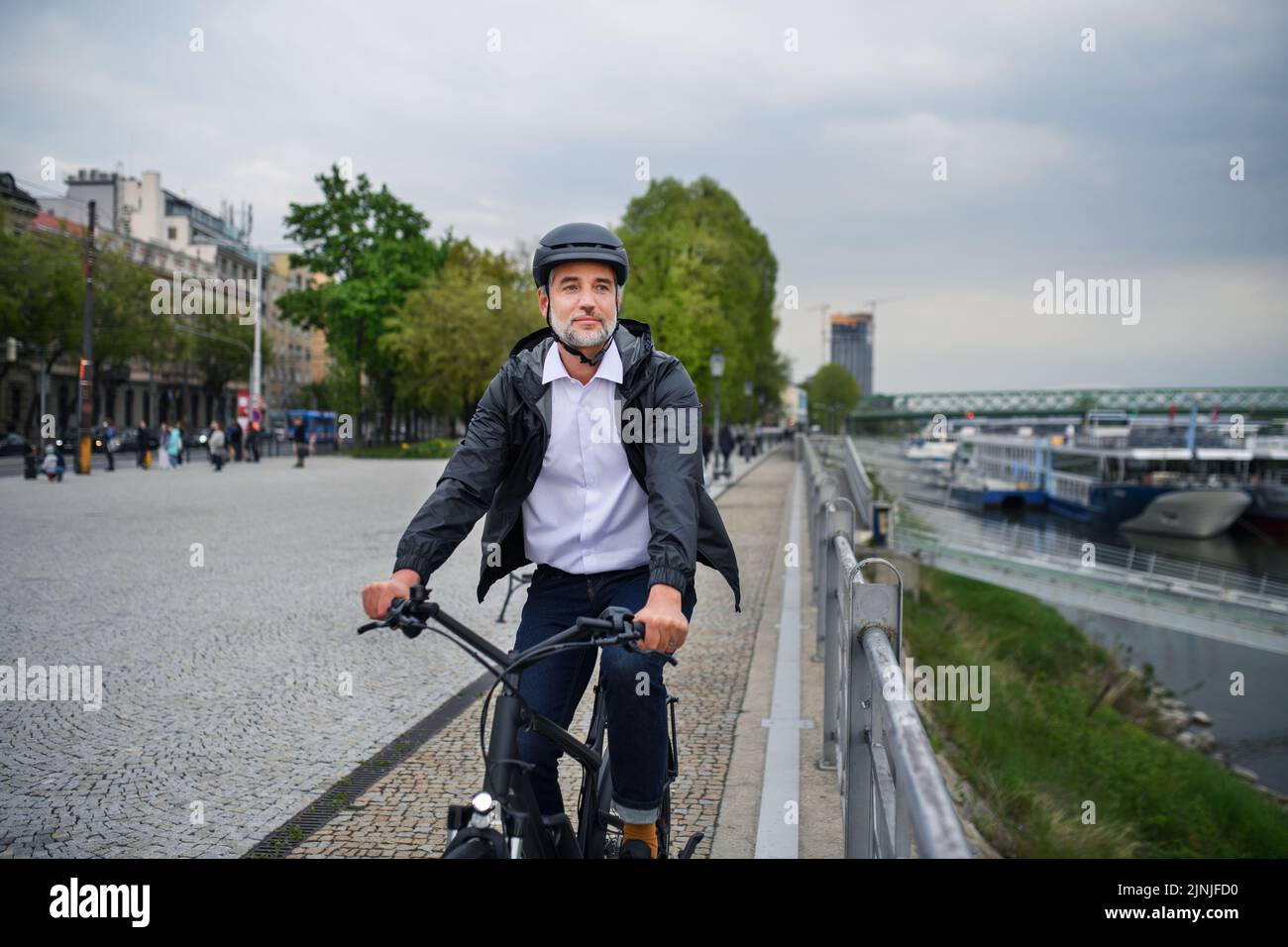 Uomo d'affari pendolari sulla strada per lavorare, in bicicletta vicino al fiume, concetto di stile di vita sostenibile. Foto Stock